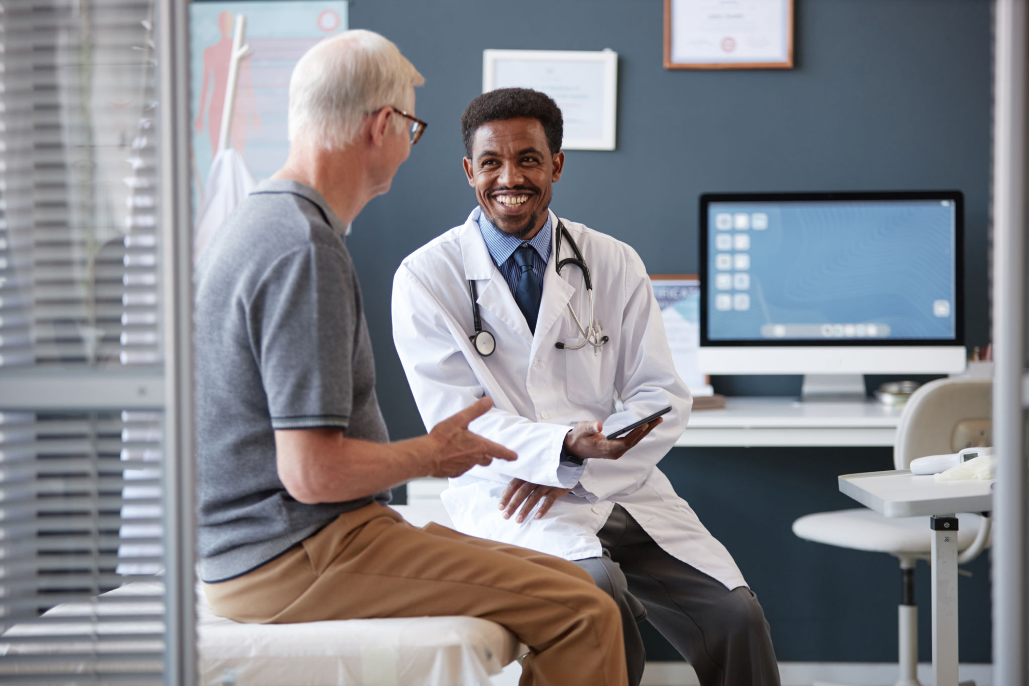 Doctor speaking with an older male patient during an in-office consultation, representing evaluation and diagnosis of prostate cancer in a clinical setting.